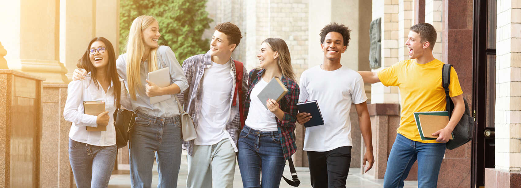 Gruppe junger, gutgelaunter Menschen mit Büchern, Blöcken und Tablets unter dem Arm