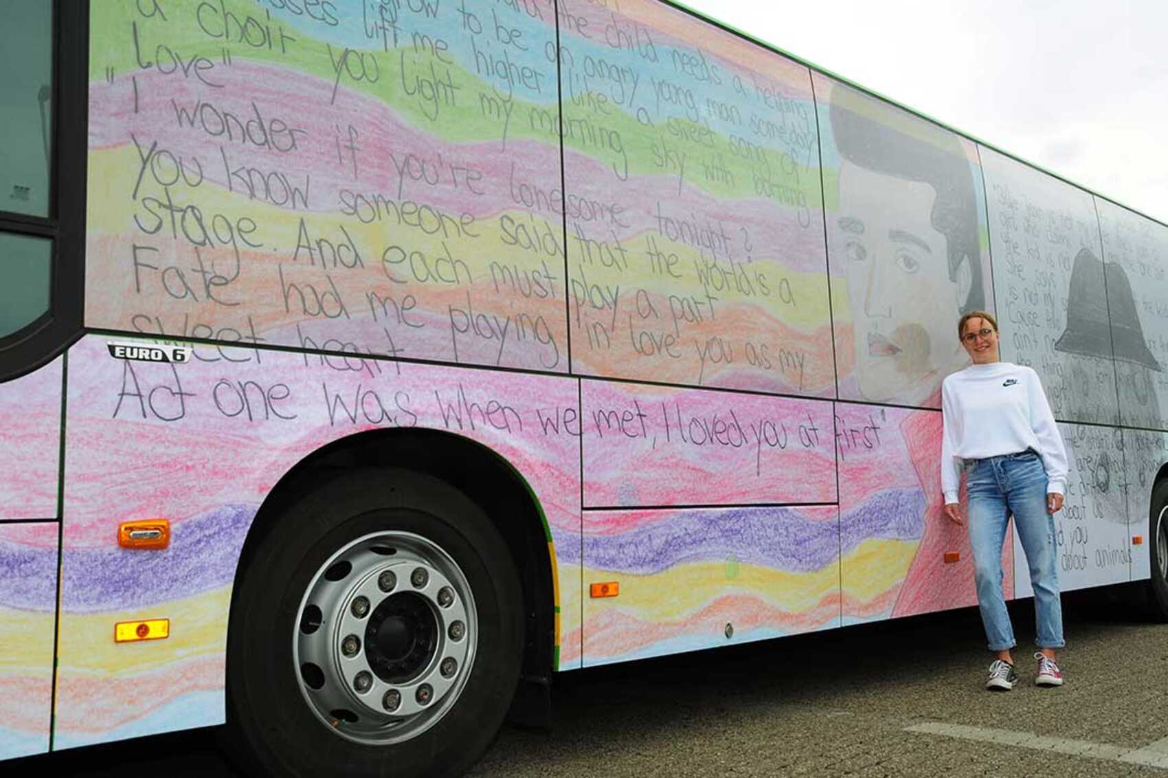 Eine Schülerin steht an der Seite eines buntbedruckten STOAG Busses